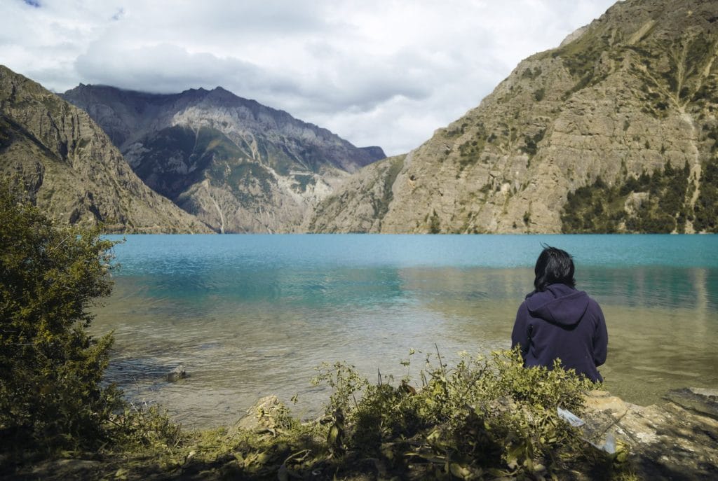 a-person-sits-by-the-serene-phoksundo-lake-in-nepal-surrounded-by-moun.lower-dolpo-treklower-dolpo-trek